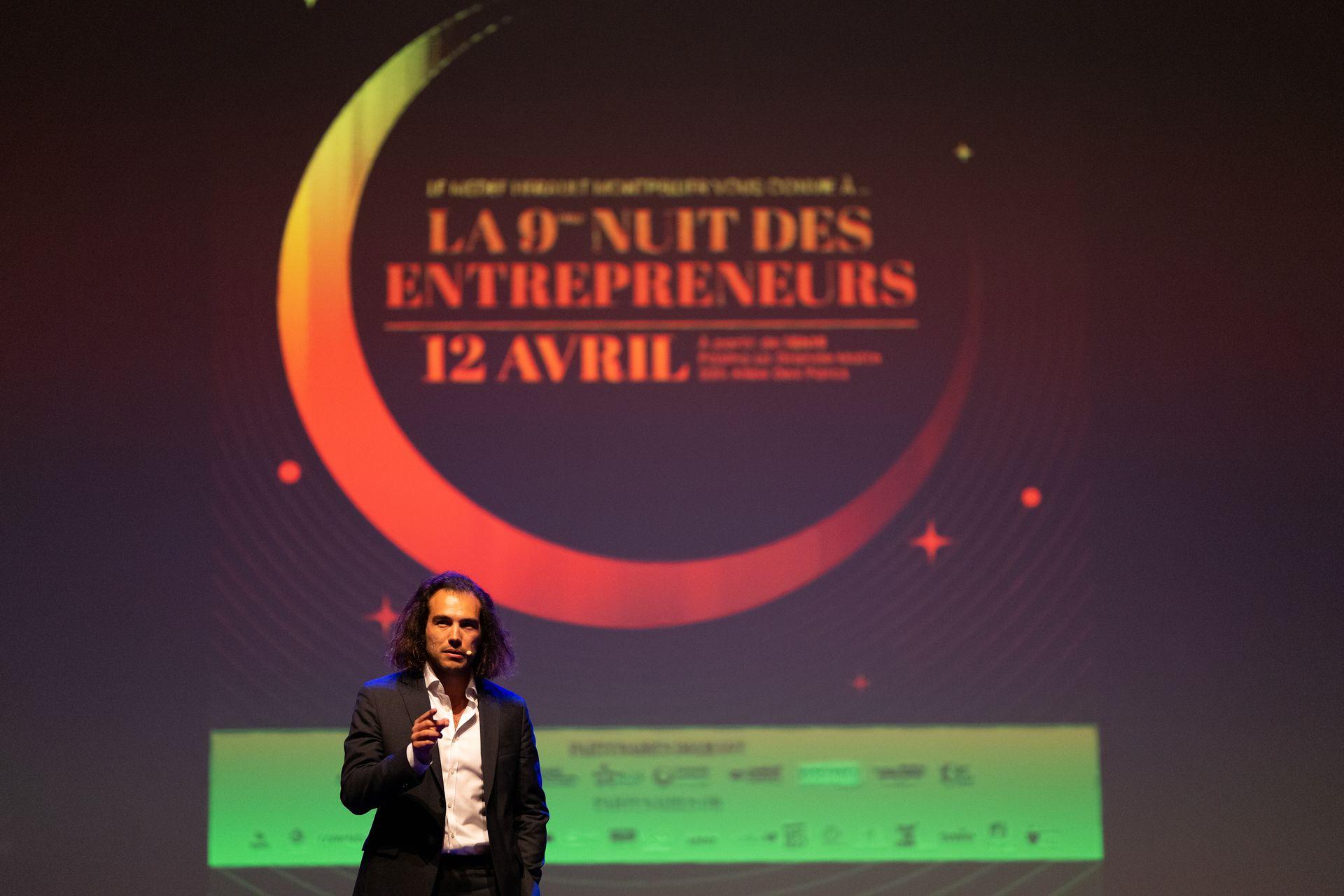 Speaker presenting at the 9th Entrepreneurs' Night event, with a backdrop displaying event details.