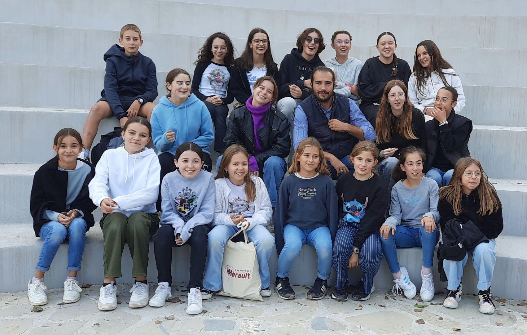 Group of people sitting on outdoor steps, wearing casual clothes and posing for a photo.