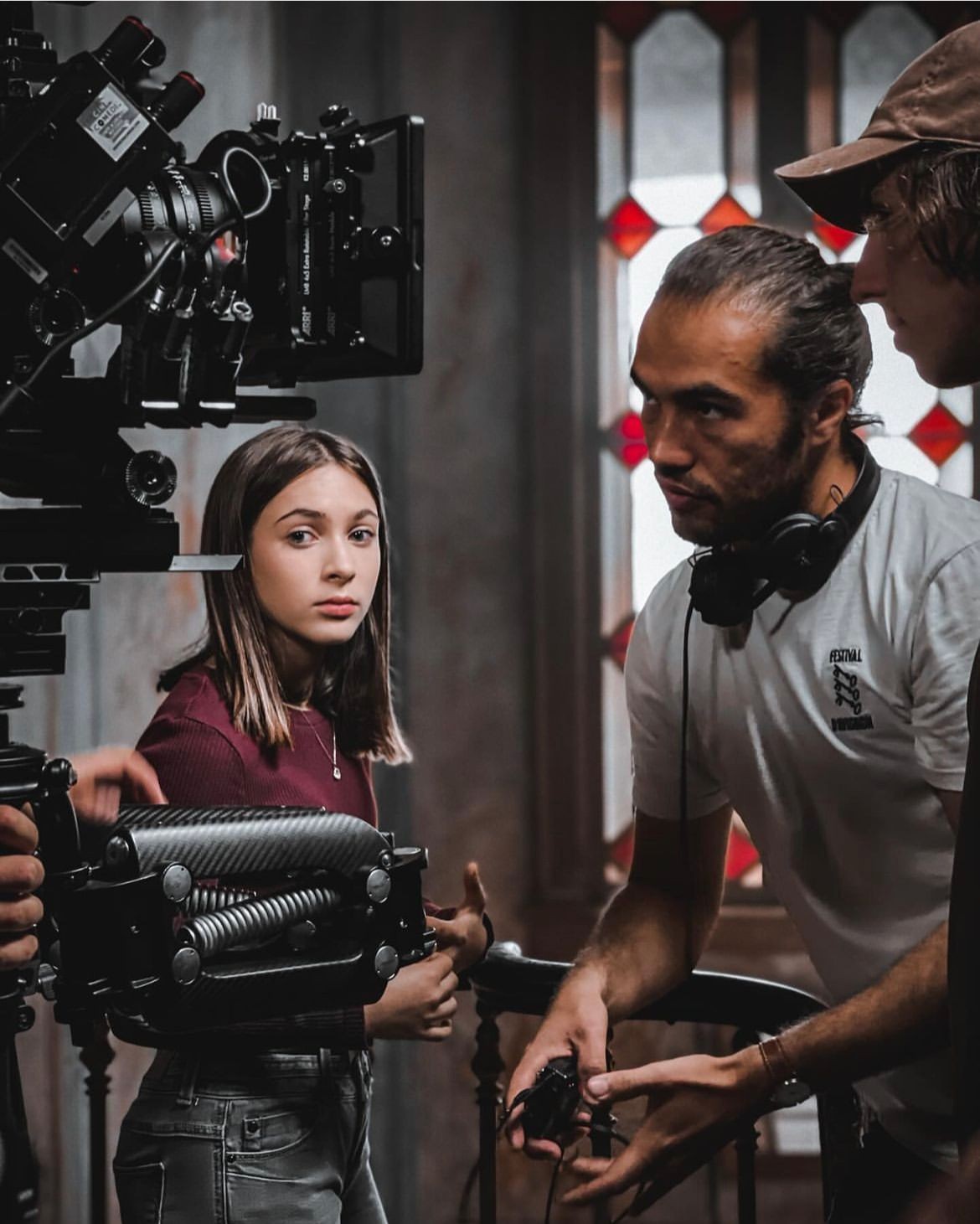 Film crew members on set adjusting camera equipment, with stained glass windows in the background.